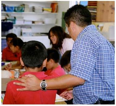 Photo: Classroom setting, man has arm around young boy in red shirt