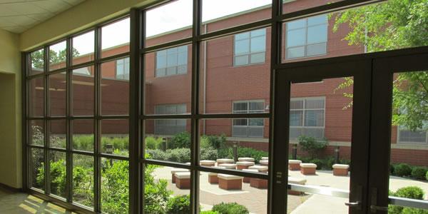 Windows display a courtyard with seating and plants with a brick building behind the courtyard. 